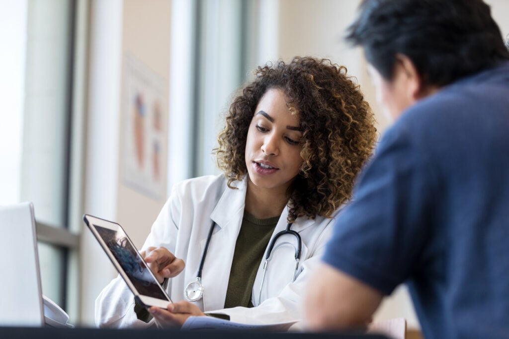 A female doctor uses a digital tablet to show prescriptions and diagnosis to a male patient.