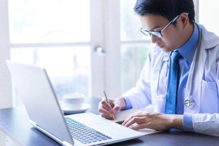 Young male doctor writing on his notebook while working from home.