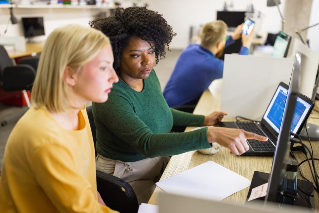 Choosing antivirus software - Two women in an office discussing while looking at their computer monitor.