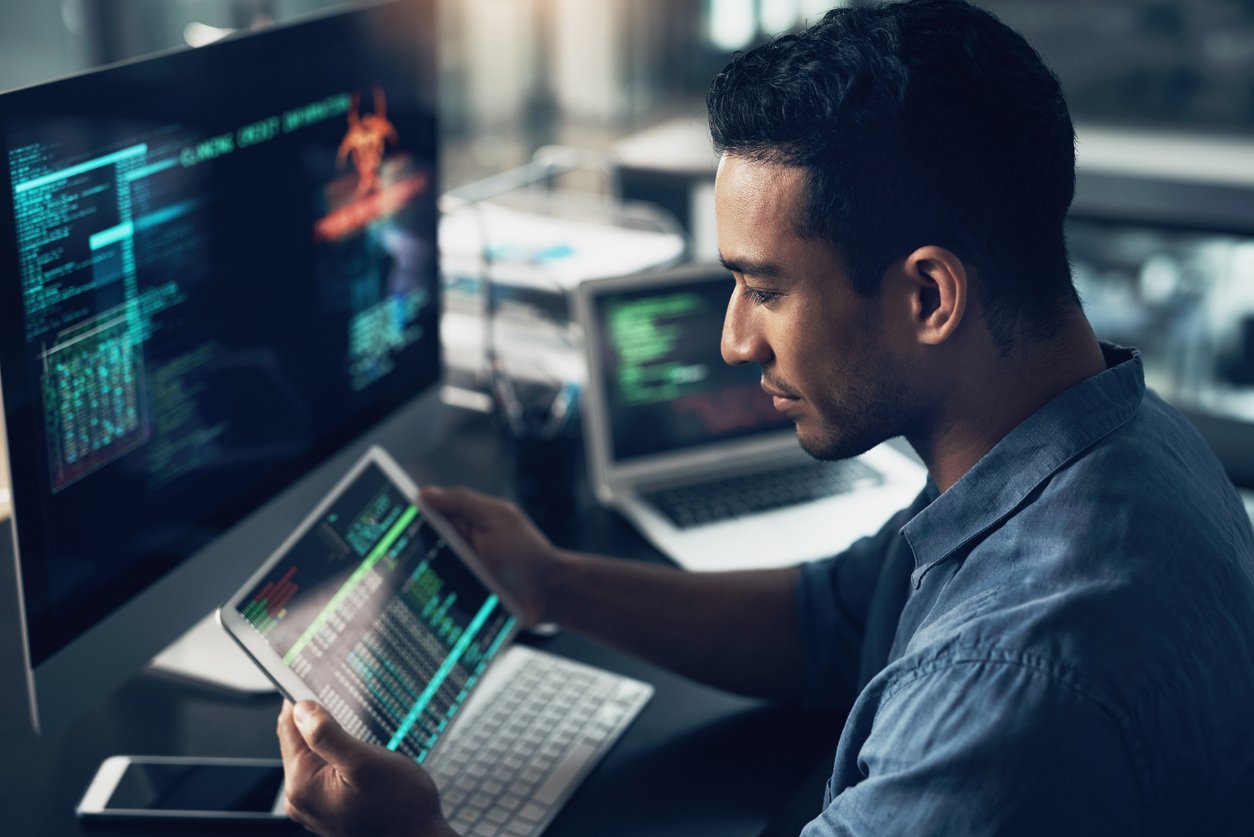 Male IT professional using a laptop and tablet device to monitor cyber attacks.