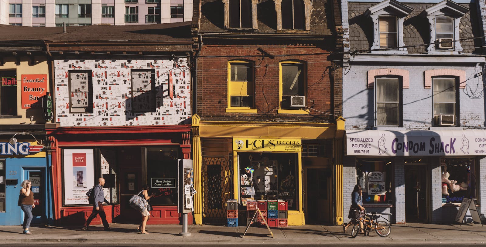 Colorful street scene with people walking past unique storefronts under sunlight.